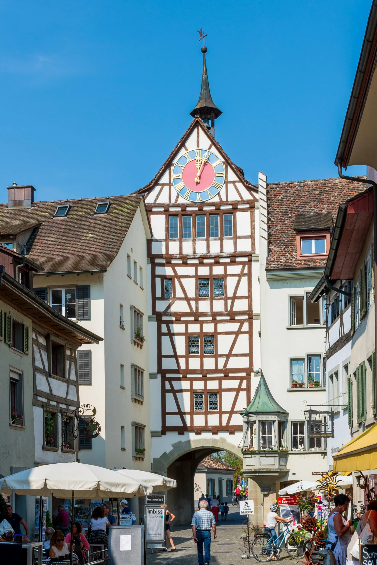 a group of people walking down a street next to tall buildings, inspired by Karl Stauffer-Bern, renaissance, huge gate, portcullis, white wall complex, brown