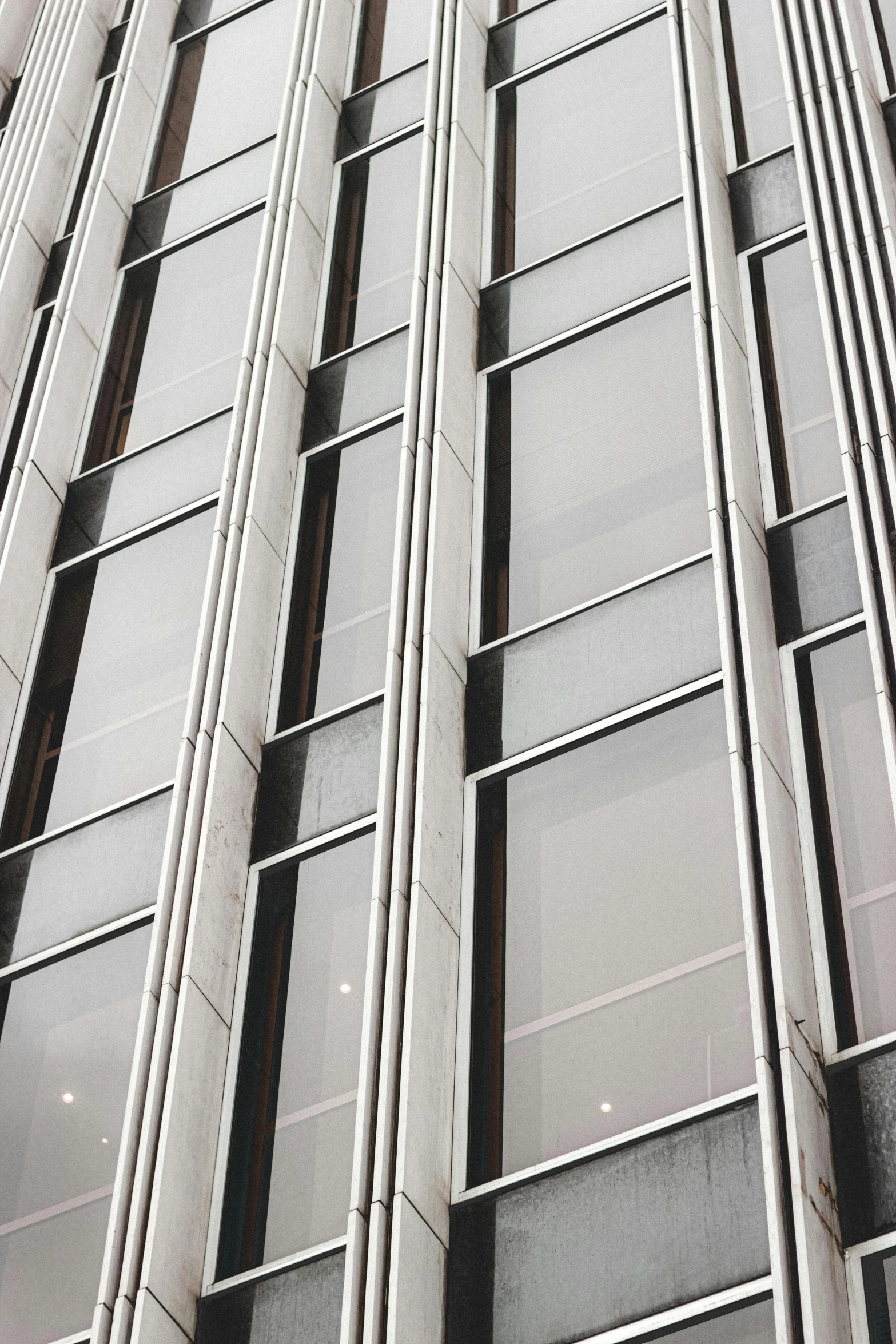 a black and white photo of a tall building, inspired by Andreas Gursky, unsplash, steel window mullions, glass window, full of silver layers, tall thin