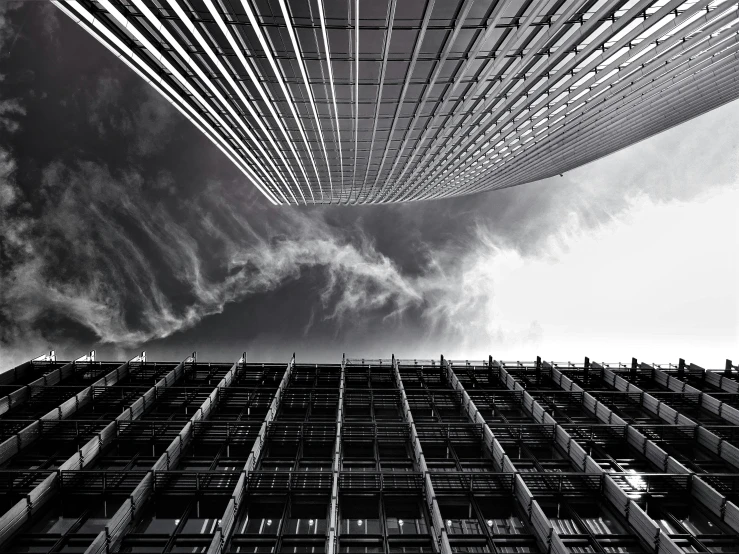a black and white photo of a tall building, a black and white photo, inspired by Zaha Hadid, pexels contest winner, clouds around, square lines, view from ground, apocalyptic architecture