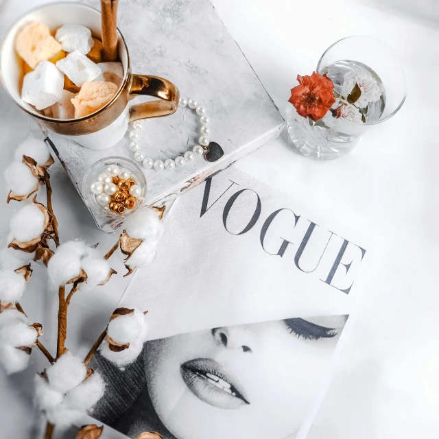 a magazine sitting on top of a bed next to a cup of coffee, by Zofia Stryjenska, baroque, vogue cover photo, jewelry pearls, white marble with gold accents, vouge style photo