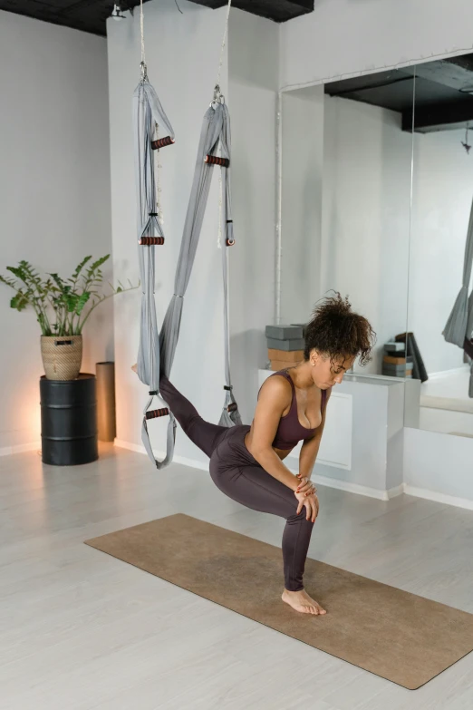 a woman doing a yoga pose on a yoga mat, by Nina Hamnett, arabesque, hanging rope, grey, squatting, brown