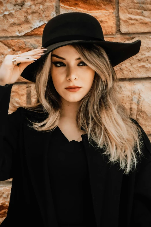 a woman wearing a black hat standing in front of a brick wall, trending on pexels, tachisme, brunette with dyed blonde hair, wearing a black robe, cl, outfit photo