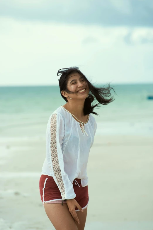 a woman standing on a beach next to the ocean, earing a shirt laughing, mahira khan as a mage, malaysian, 8 5 mm photograph