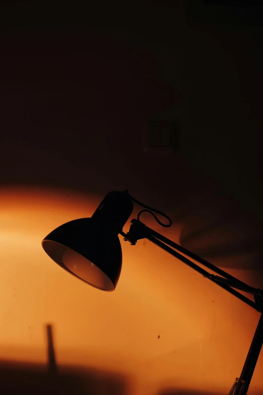 a desk lamp sitting on top of a wooden desk, by Ian Fairweather, pexels, light and space, silhouette :7, orange and black, up close, warm color