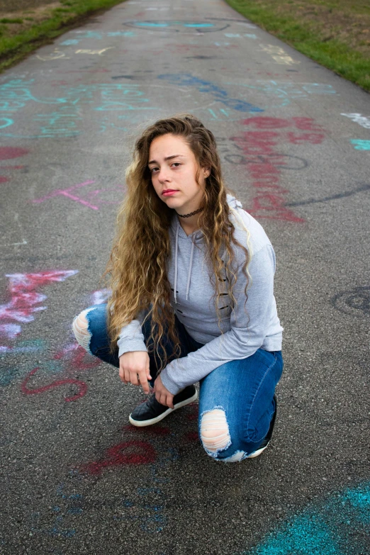 a girl sitting on a skateboard in the middle of a road, trending on pexels, graffiti, portrait sophie mudd, curls, grey hoodie, queer woman