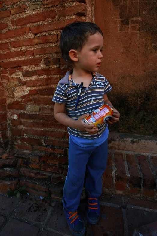 a young boy standing in front of a brick wall, a picture, inspired by Steve McCurry, condorito, juice, toddler, ::