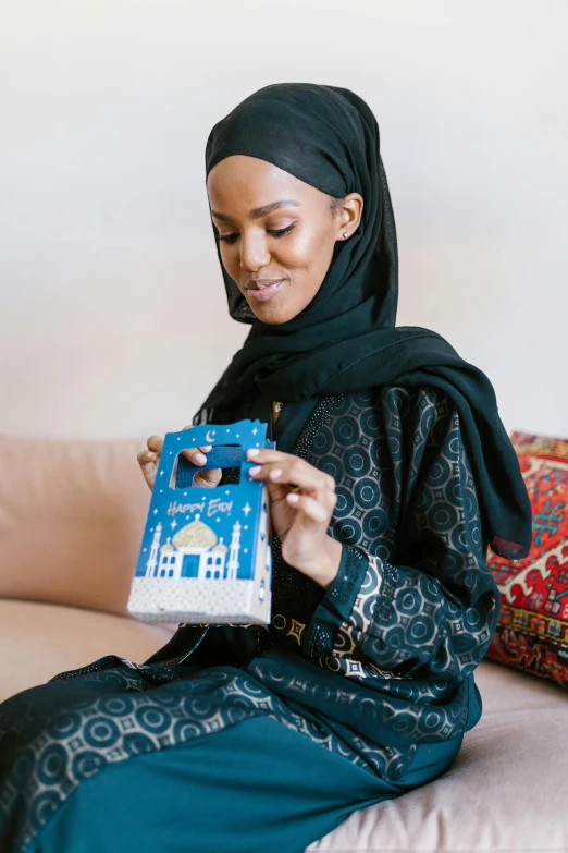 a woman sitting on a couch holding a book, hurufiyya, robot model kit, somali woman, with blue light inside, holding a bell