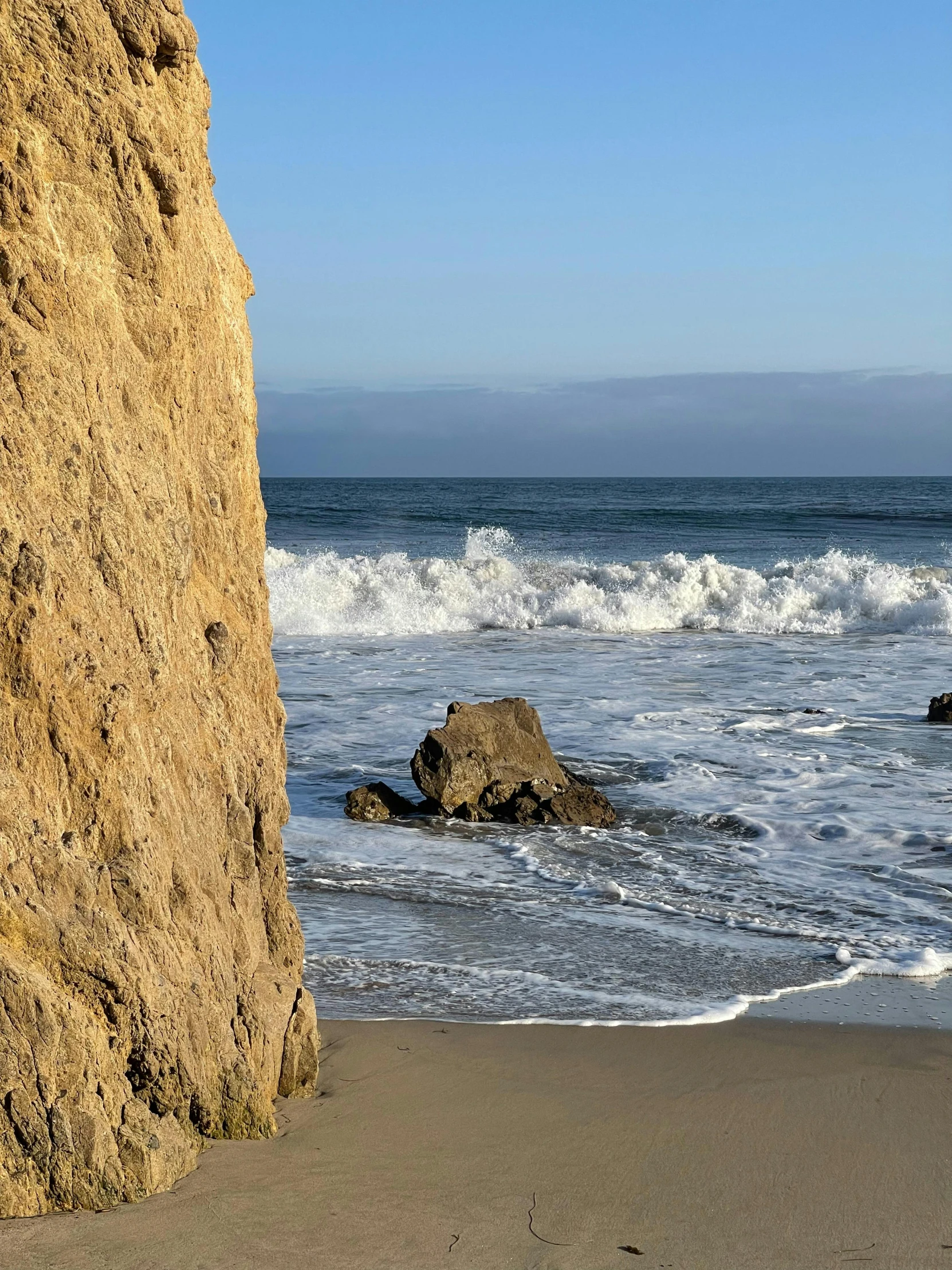 a man riding a surfboard on top of a sandy beach, rock walls, 5 feet away, pch, zoomed in