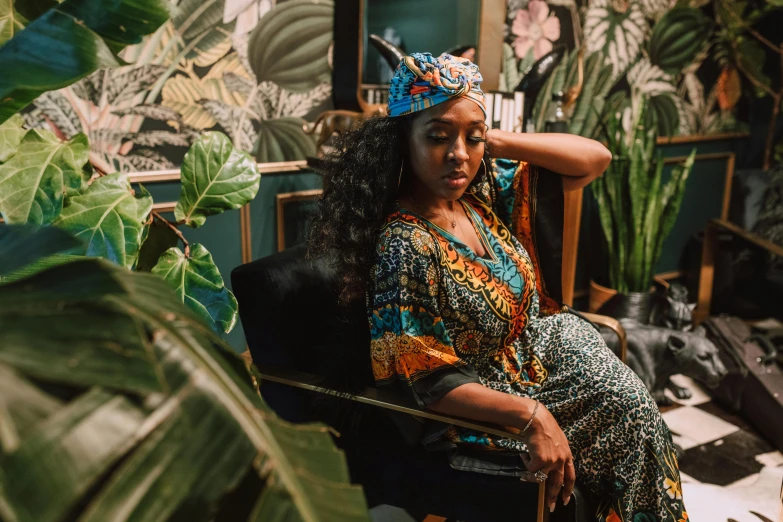 a woman sitting in a chair with a crown on her head, pexels contest winner, afrofuturism, lush oasis, patterned clothing, sitting in a lounge, thumbnail