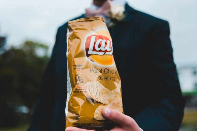 a man in a suit holding a bag of chips, inspired by Chippy, unsplash, wedding, liam brazier, instagram post, rectangle