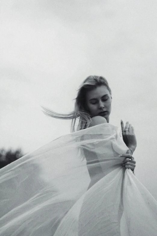 a black and white photo of a woman in a wedding dress, inspired by irakli nadar, tumblr, cloak flittering in the wind, young blonde woman, sheer fabrics, sky witch