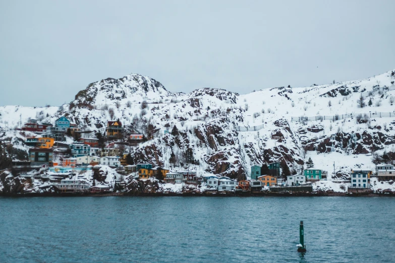 a mountain covered in snow next to a body of water, by Ejnar Nielsen, pexels contest winner, art nouveau, fishing village, harbor, in muted colours, gungnir