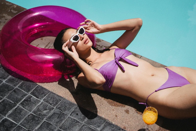 a woman in a purple bikini laying next to a pool, trending on pexels, inflatable, implanted sunglasses, photoshoot for skincare brand, bella poarch