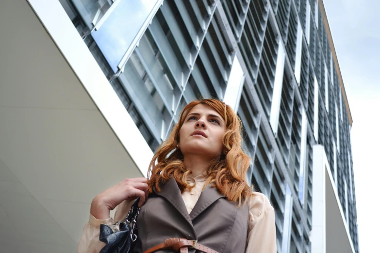 a woman standing in front of a tall building, pexels contest winner, renaissance, wearing a worn out brown suit, maiden with copper hair, people at work, cinematic outfit photo