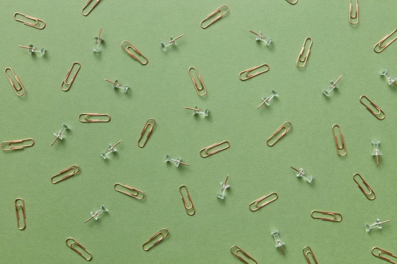 a bunch of paper clips sitting on top of a green surface, by Emma Andijewska, trending on pexels, with crystals on the walls, repeating pattern, bullet shells flying, thin gold details