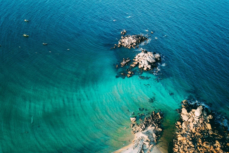 a view of a body of water from a bird's eye view, by Lee Loughridge, pexels contest winner, teal color graded, rocky seashore, manly, beautifully lit