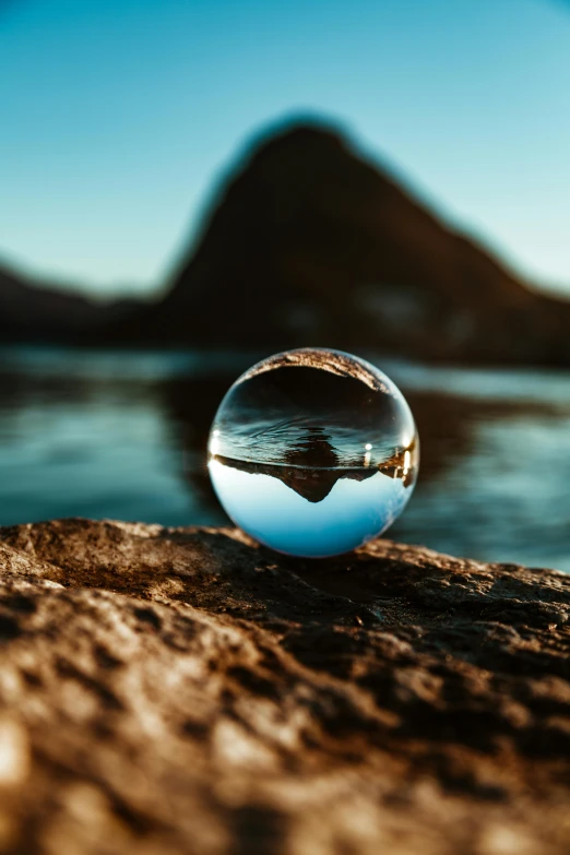 a glass ball sitting on top of a rock, body of water, mountain water