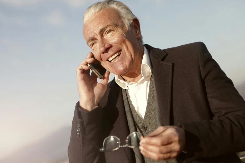 a man in a suit talking on a cell phone, a photo, by John Murdoch, white hair floating in air, promo image, old man, sunny day