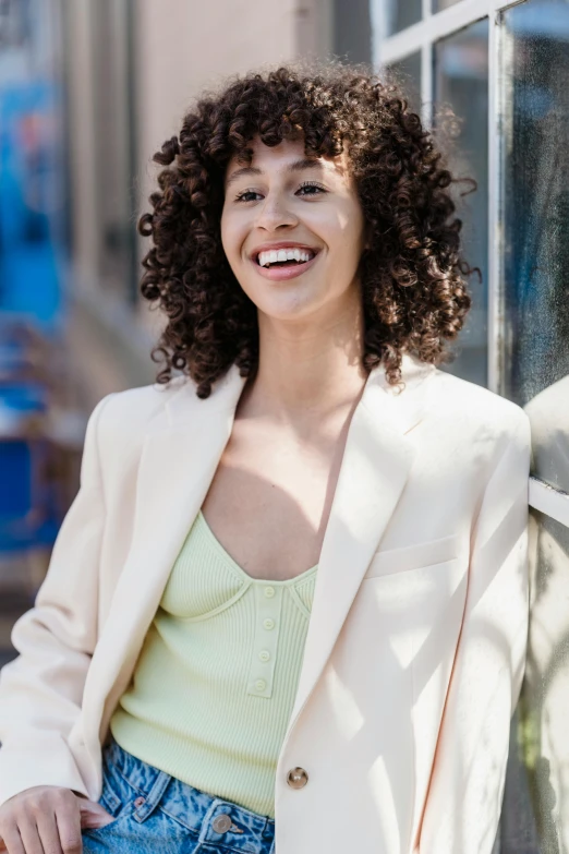 a woman with curly hair leaning against a wall, trending on pexels, wearing a light - pink suit, fair olive skin, portrait of happy a young woman, al fresco