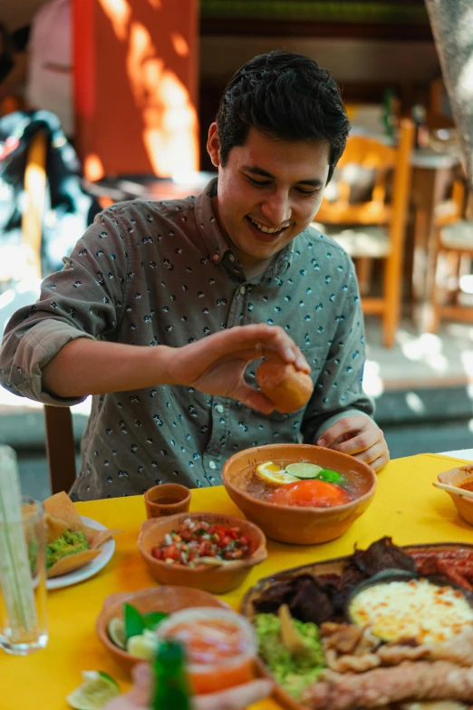 a man sitting at a table full of food, tlaquepaque, blending, young spanish man, bowl filled with food