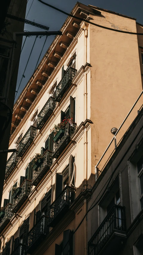 a tall building with balconies on the side of it, by Pablo Rey, pexels contest winner, neoclassicism, shady alleys, low quality photo, golden light, exterior photo