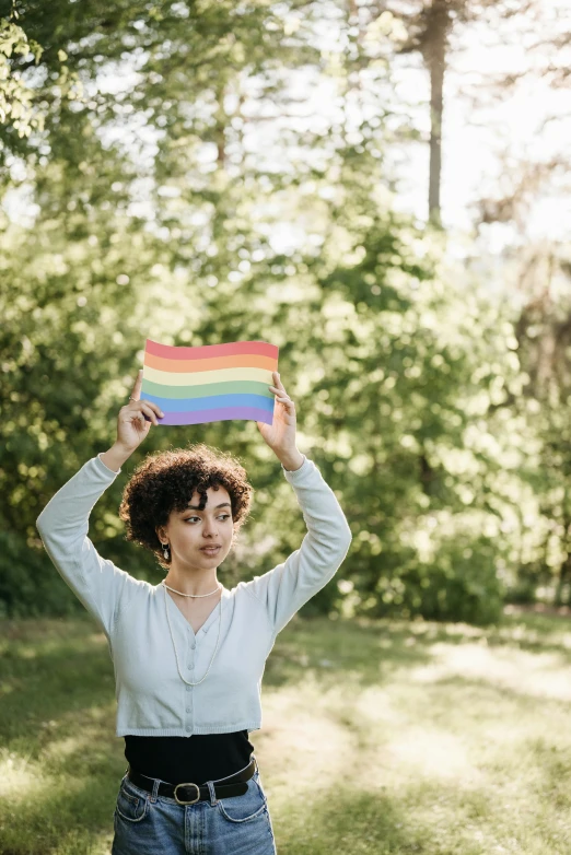 a woman holding a rainbow flag over her head, trending on pexels, renaissance, in a park, woman his holding a sign, ashteroth, charts