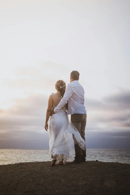 a man and a woman standing on top of a beach, wedding photography, looking out at the ocean, back - lit, resting