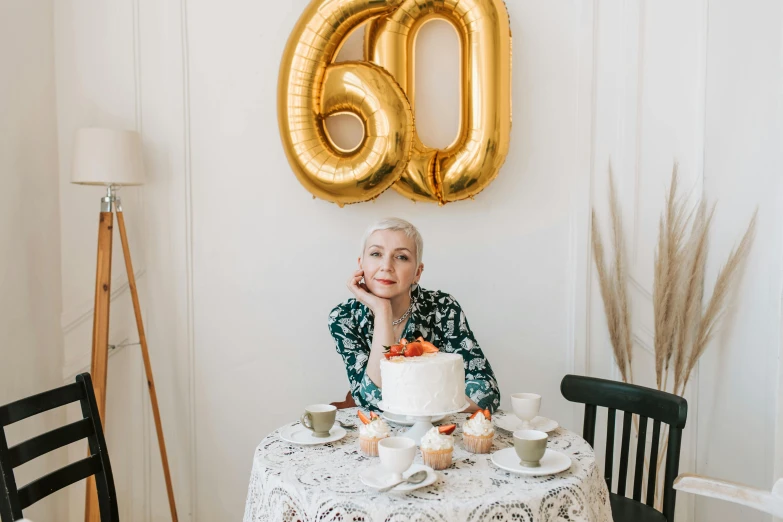 a woman sitting at a table with a cake, by Emma Andijewska, trending on unsplash, he is about 6 0 years old, balloon, very very very pale skin, celebration of coffee products