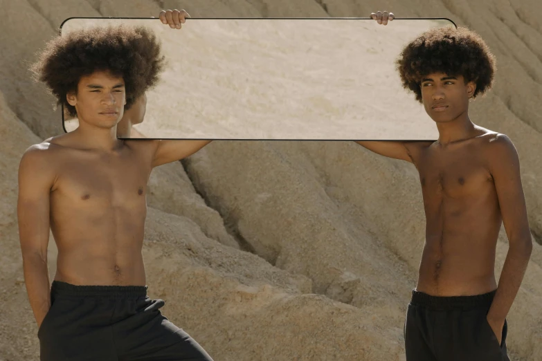 a couple of men standing next to each other holding a sign, an album cover, unsplash, conceptual art, afro hair, his body buried in the sand, 2 0 2 1 cinematic 4 k framegrab, 14 yo berber boy