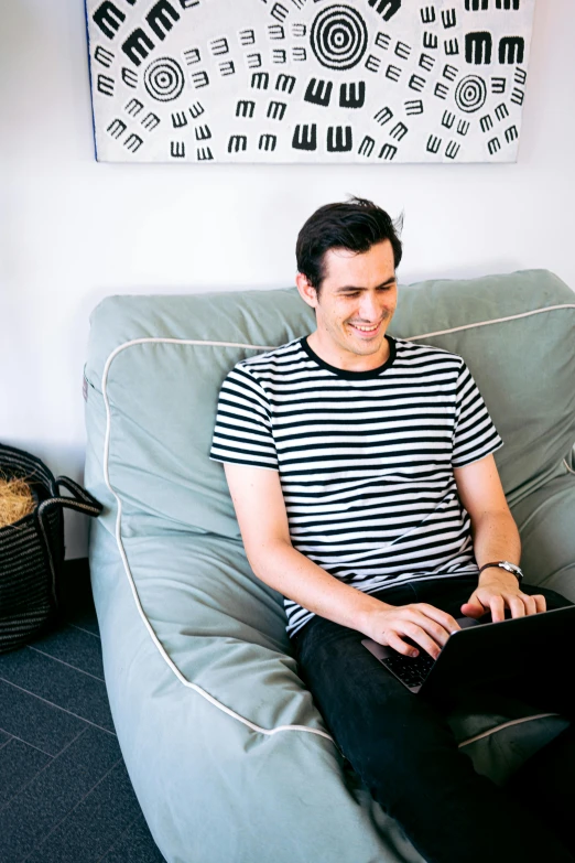 a man sitting on a couch using a laptop, inspired by Jason Felix, happening, small and cosy student bedroom, smiling man, nathan for you, premium quality