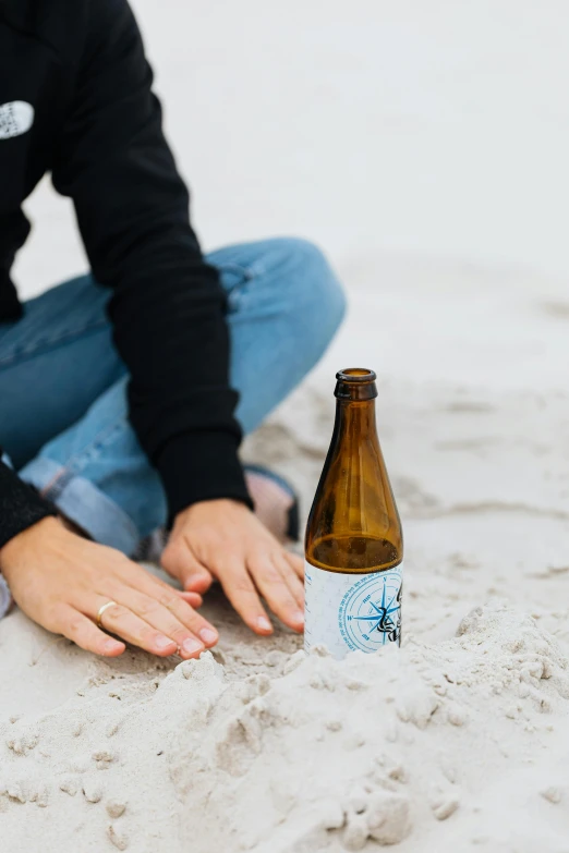 a woman sitting on a beach next to a bottle of beer, by Tuvia Beeri, unsplash contest winner, on white background, blue, head down, carefully crafted