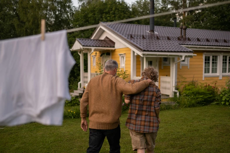 a man and a woman standing in front of a house, by Anato Finnstark, pexels contest winner, symbolism, laundry hanging, parents watching, midsummer, promo image