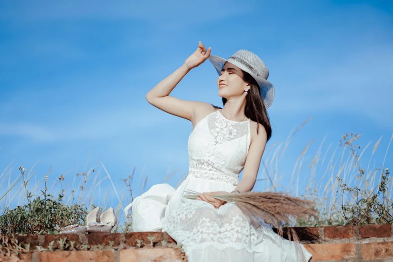 a woman in a white dress and hat sitting on a brick wall, pexels contest winner, clear blue sky vintage style, 15081959 21121991 01012000 4k, wearing a wedding dress, hoang long ly