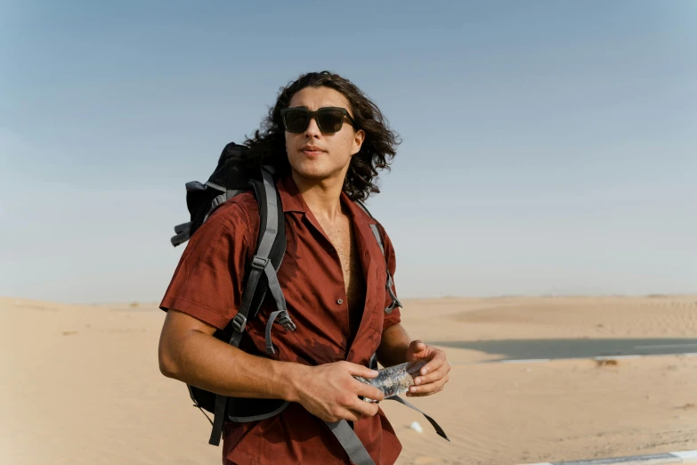 a man standing on top of a sandy beach, avan jogia angel, in the desert beside the gulf, head and shoulders 8 0 mm camera, a man wearing a backpack