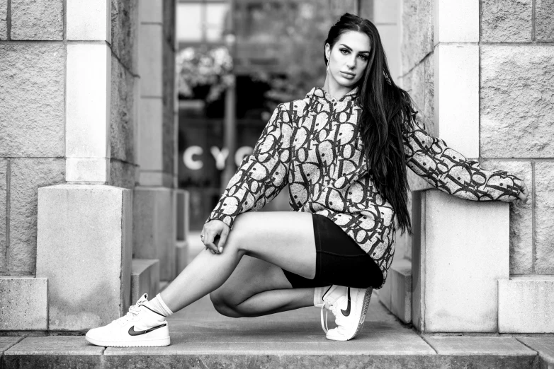 a woman sitting on the steps of a building, a black and white photo, pexels, lyco art, charli xcx, athletic fashion photography, patterned clothing, casual pose