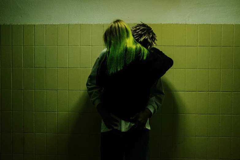 a woman with green hair leaning against a wall, an album cover, inspired by Elsa Bleda, pexels contest winner, antipodeans, two men hugging, faceless people dark, dayglo, in a bathroom
