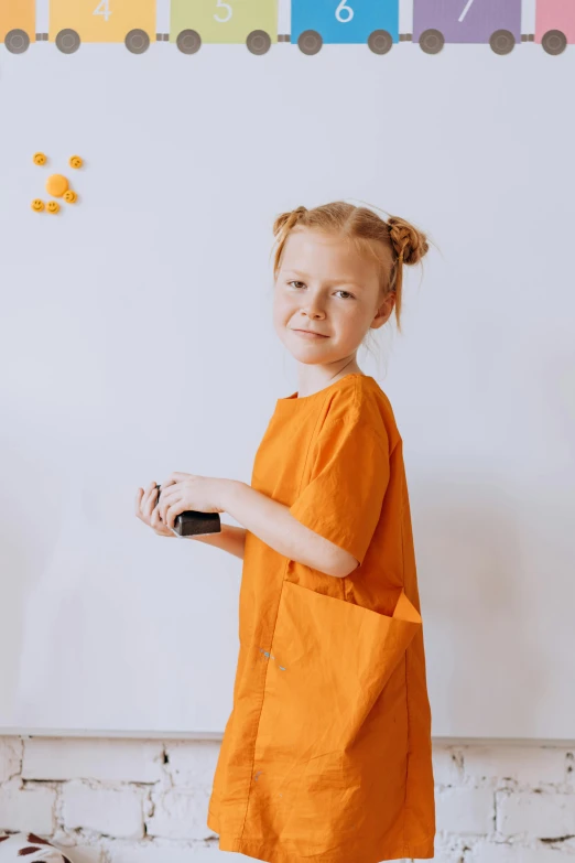 a little girl standing in front of a whiteboard, pexels contest winner, antipodeans, wearing orange prison jumpsuit, wearing nanotech honeycomb robe, with two front pockets, nurse girl