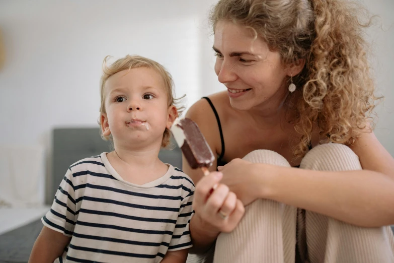 a woman sitting next to a child holding a popsicle, pexels contest winner, some chocolate sauce, avatar image, australian, 1 4 9 3