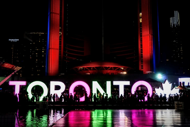 people standing in front of the toronto sign at night, by Julia Pishtar, pexels contest winner, a brightly colored, drake, dan flavin, promo image