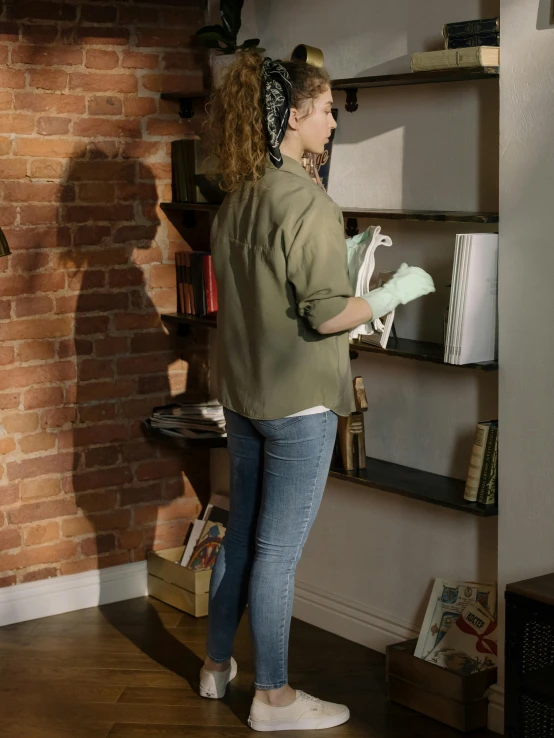 a woman standing in front of a bookshelf holding a book, a colorized photo, trending on reddit, ( ( ( wearing jeans ) ) ), reflective visor, inspect in inventory image, hyperrealism style