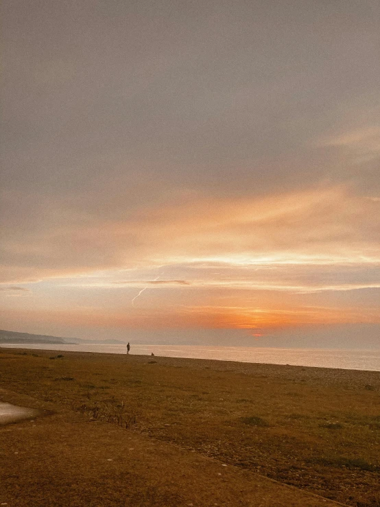 a man flying a kite on top of a sandy beach, a picture, by John Henderson, unsplash contest winner, in a sunset haze, panoramic photography, taken on iphone 1 3 pro, omaha beach