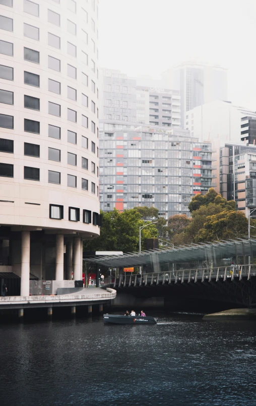 a boat traveling down a river next to tall buildings, by Lee Loughridge, pexels contest winner, melbourne, trending on vsco, curved bridge, slight overcast