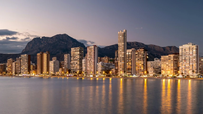 a large body of water surrounded by tall buildings, pexels contest winner, costa blanca, in the evening, mountains and ocean, foil