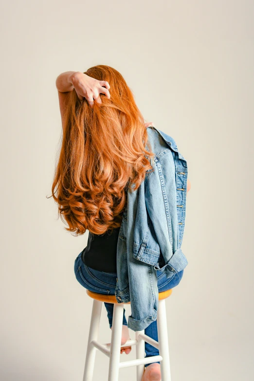 a woman with long red hair sitting on a stool, trending on pexels, denim jacket, hands in her hair. side-view, voluminous sleeves, back view. nuri iyem