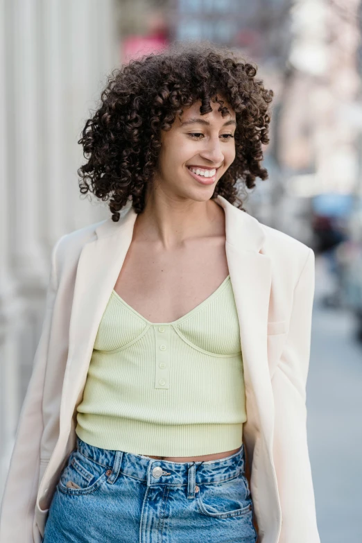 a woman with curly hair walking down the street, pale green halter top, wearing a blazer, wearing : tanktop, curated collections