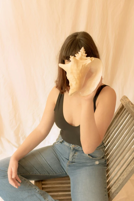 a woman sitting on a bench with a shell in her hand, an album cover, pexels contest winner, plain background, bralette, headshot profile picture, indoor picture