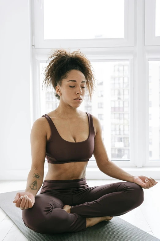 a woman sitting on a yoga mat in front of a window, by Nina Hamnett, trending on pexels, renaissance, portrait of vanessa morgan, breathing, physical : tinyest midriff ever, brown