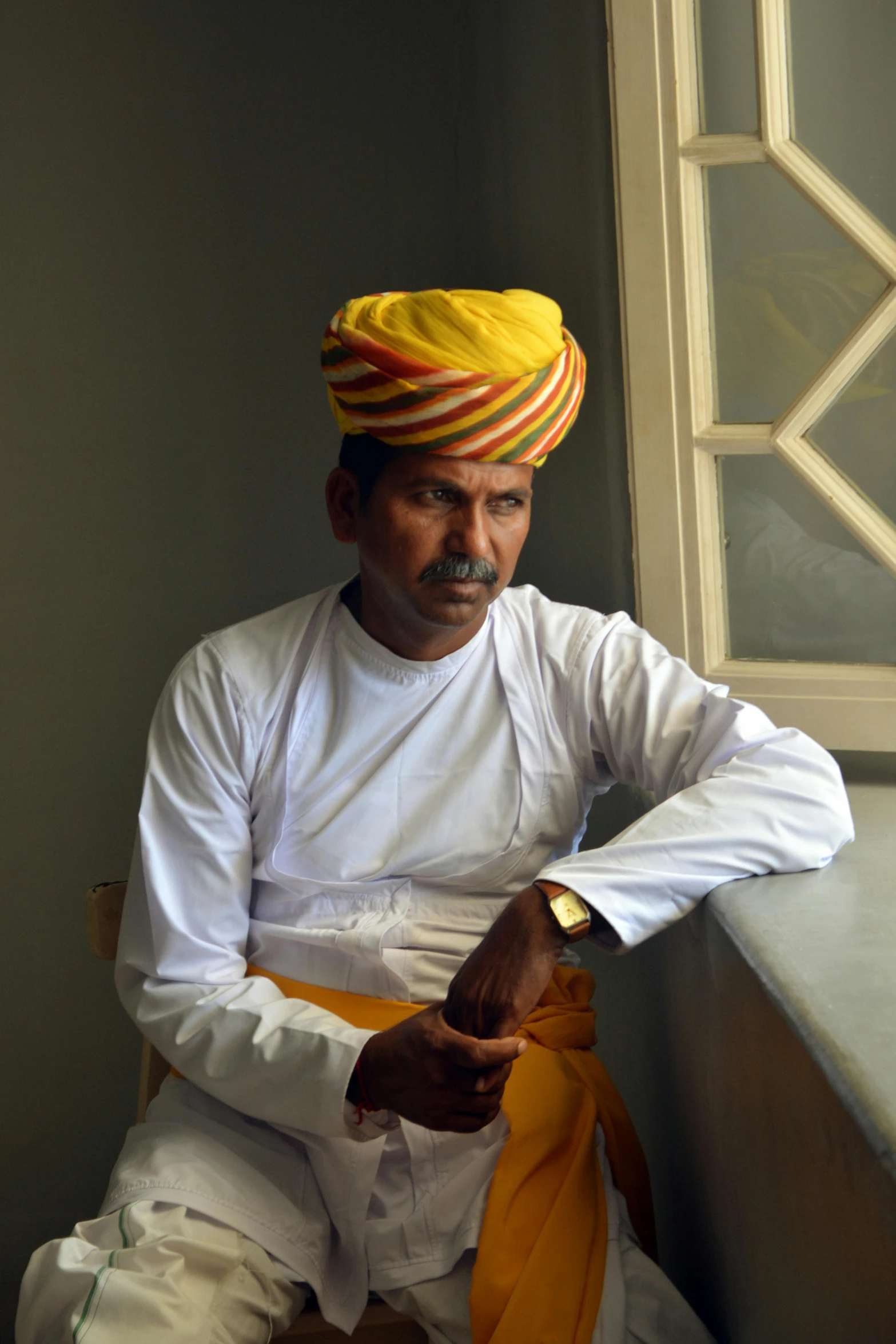 a man in a turban sitting by a window, by Rajesh Soni, yellow, square, afar, candid photograph