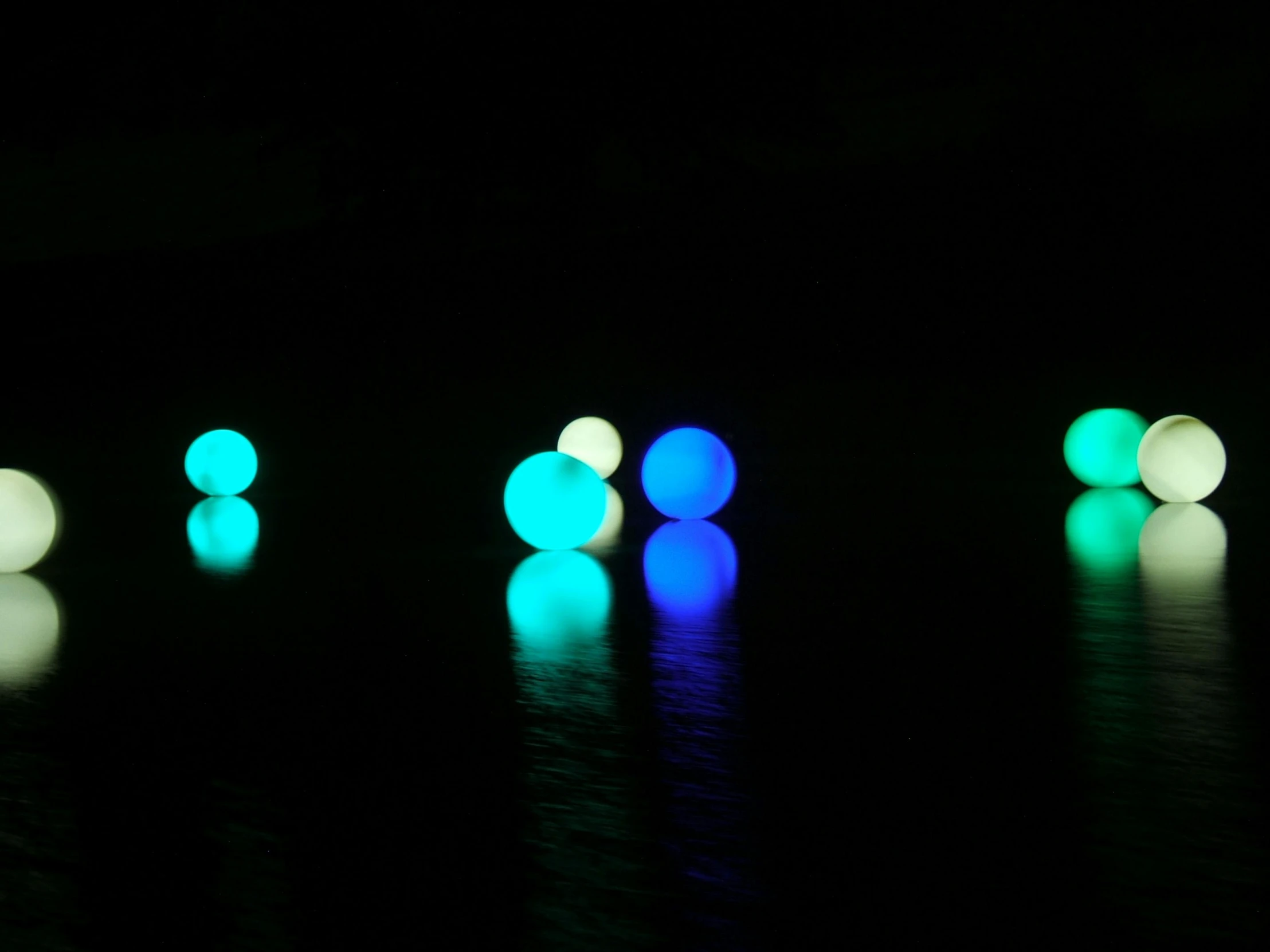 a group of glowing balls sitting on top of a table, inspired by Bruce Munro, interactive art, lake blue, coloured, on a lake, floating. greenish blue