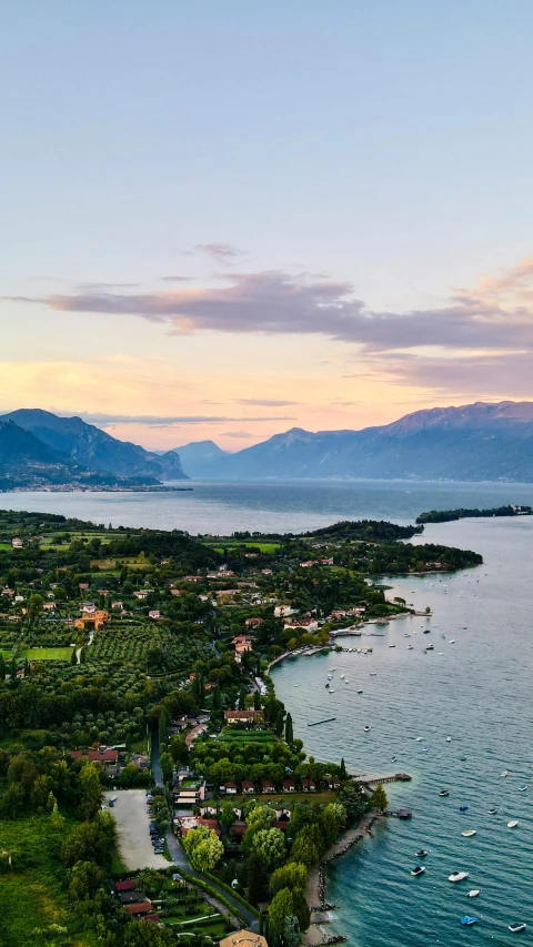 a large body of water next to a lush green hillside, inspired by Tommaso Redi, pexels contest winner, evening at dusk, the alps are in the background, islands, aerial view of a city